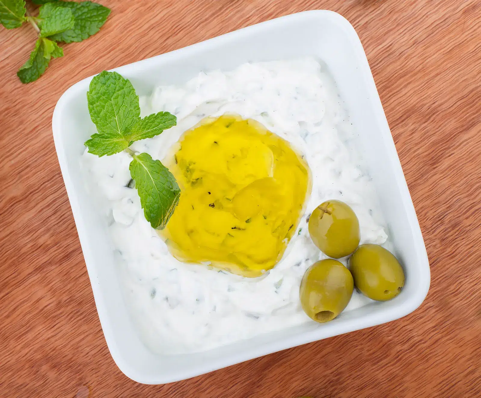 Tzatziki mit Olivenöl, Oliven und frischer Minze in einer Schale